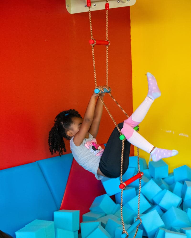 A child exploring rope movement equipment above the blue foam pit in the original Sensory Escape gym.